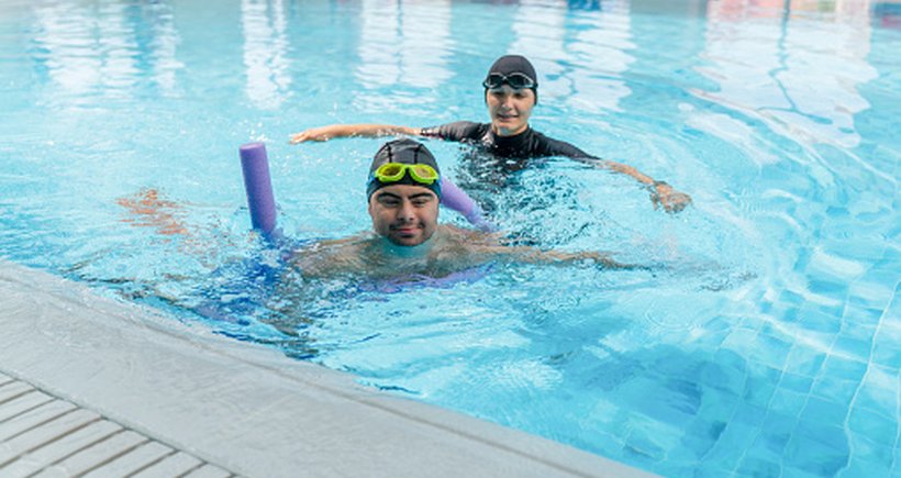A person having a fun swimming lesson with their support worker in a pool, using a floater for support.